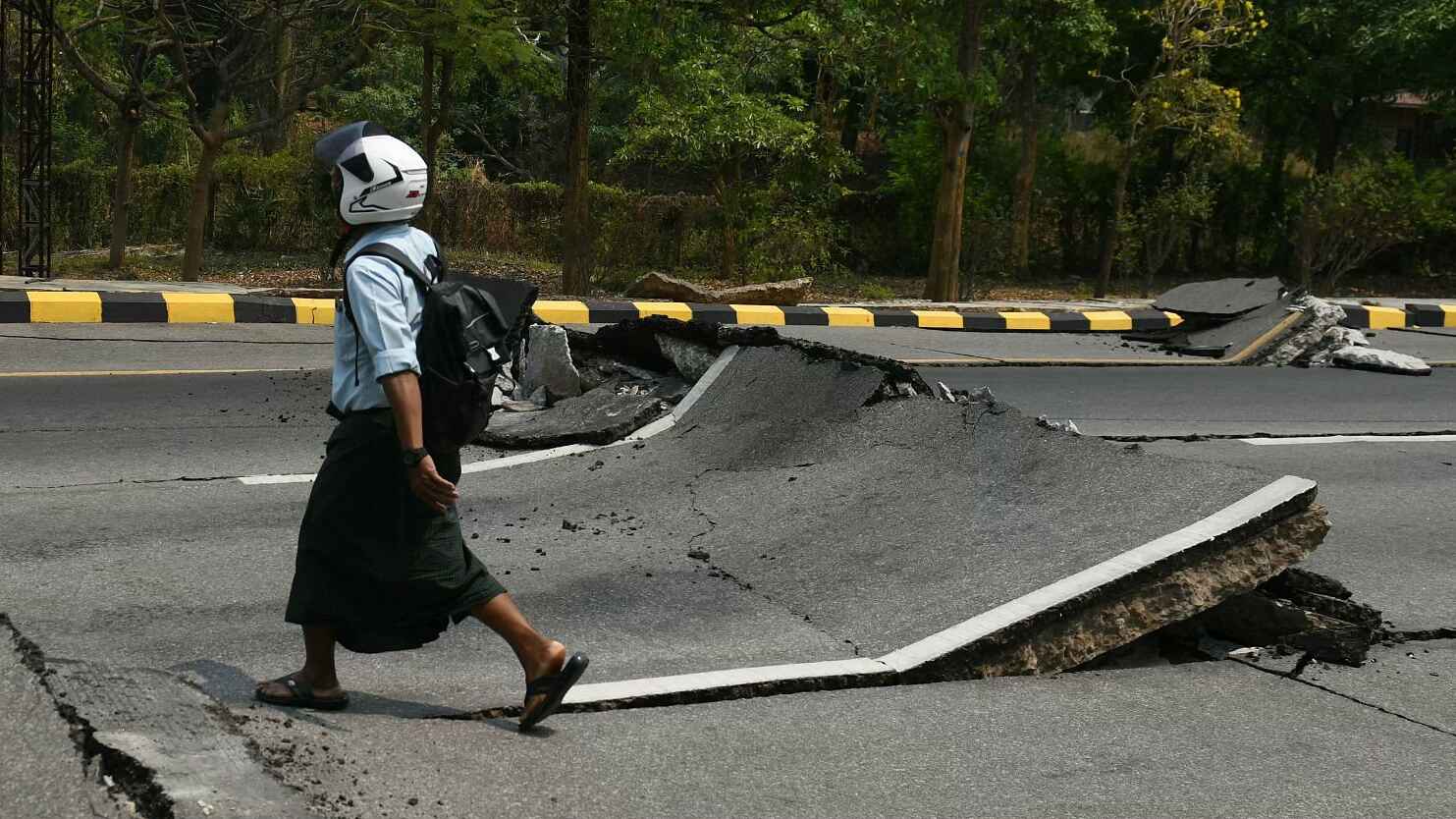 ভূমিকম্পে ক্ষতিগ্রস্থ রাস্তায় হেলমেট পড়ে হাঁটছে এক নাগরিক।